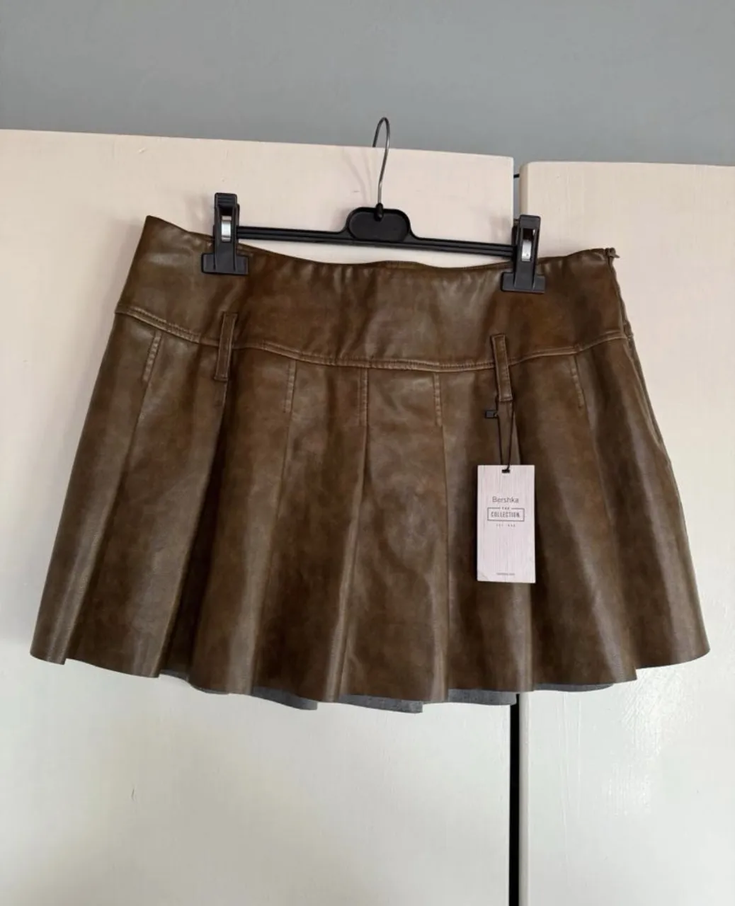 Pollera corta de cuero sintético marrón con tablas. Tiene presillas en la cintura.