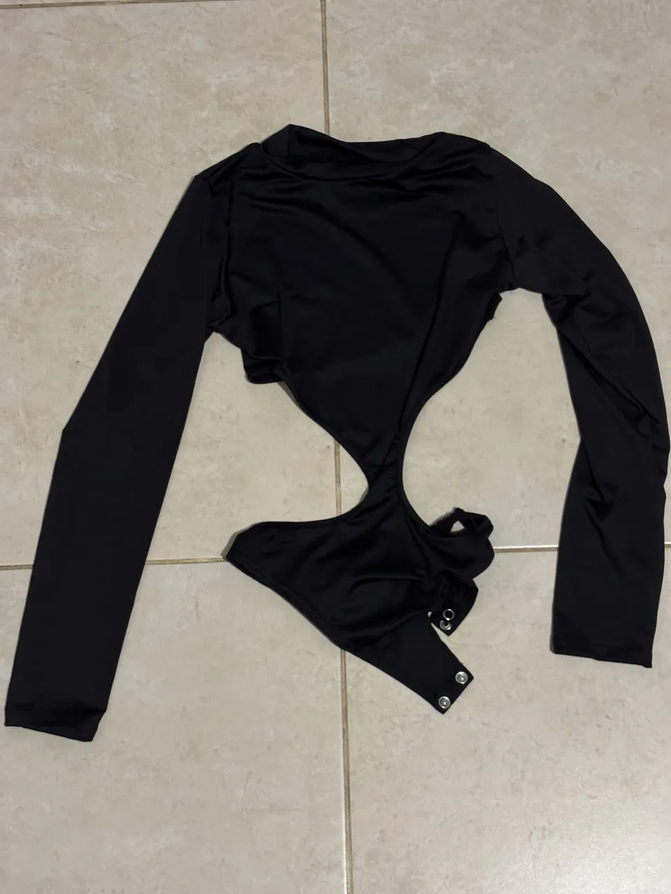 Body negro de manga larga con recortes y detalles de broches en la parte inferior. Un diseño audaz y moderno, perfecto para destacar en cualquier salida.