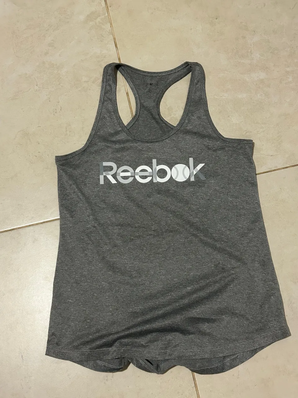 Musculosa deportiva gris de Reebok, ideal para entrenar o para un look casual y cómodo. Presenta el logo de la marca estampado en el frente.
