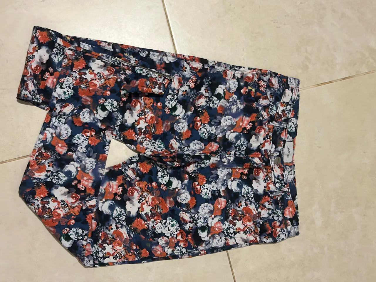 Pantalón de jean tiro alto con estampa floral vibrante en tonos azules, rojos y blancos. Posee cierre y bolsillos, ideal para un look casual y canchero.