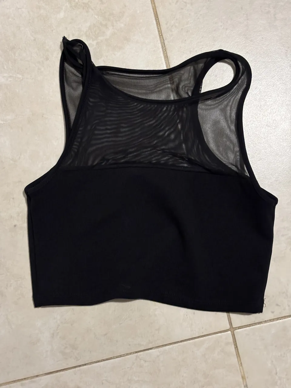 Top deportivo negro con detalles de red en la parte superior. Ideal para entrenamientos o para un look casual y moderno.