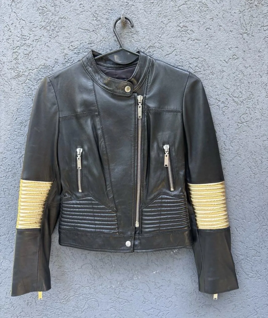 Campera de cuero negra con detalles dorados en las mangas. Cierre central y bolsillos delanteros con cierres metálicos.