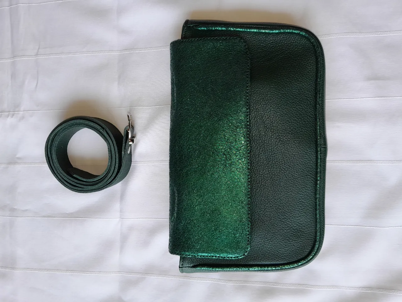 Cartera verde con correa desmontable. Posee un bolsillo frontal con solapa y cierre de broche.