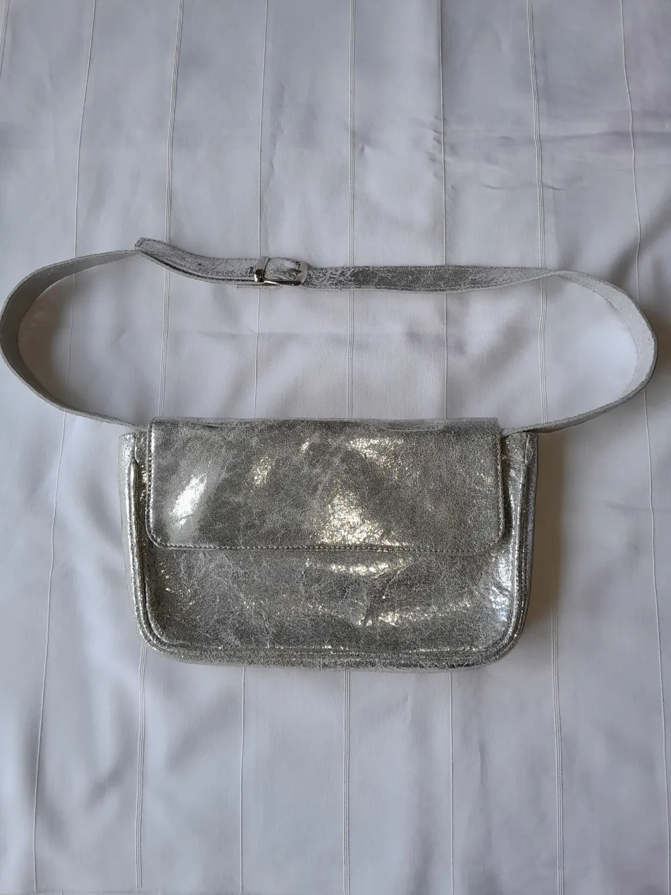 Riñonera plateada con textura metalizada y correa ajustable con hebilla.