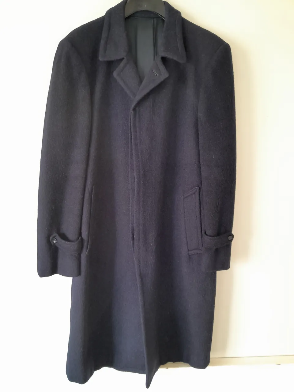 Tapado de paño azul marino, largo hasta la rodilla, con cuello solapa, tres botones al frente y dos bolsillos laterales con tapa. En las mangas tiene un detalle de botón.