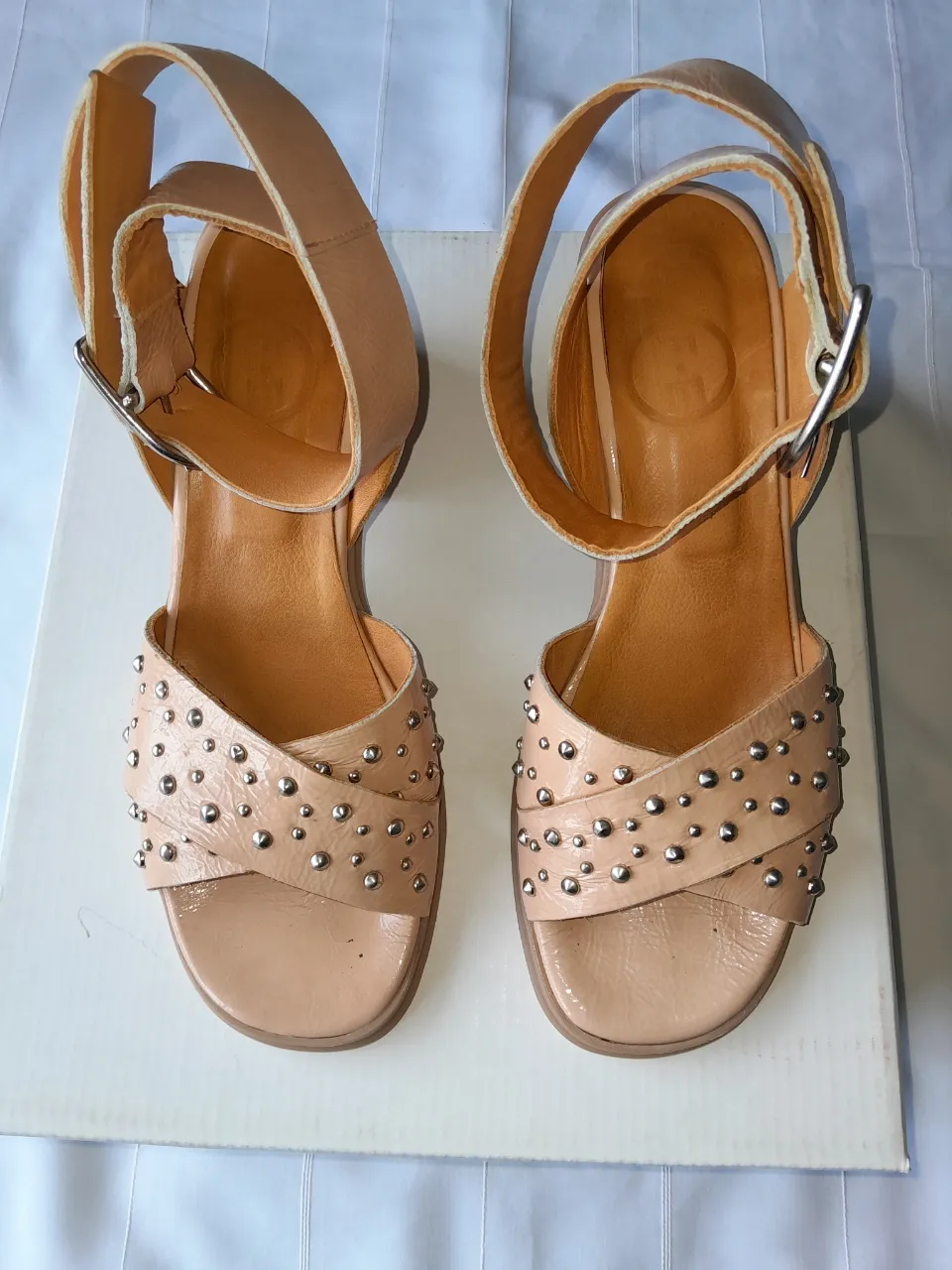 Sandalias bajas color nude con tiras cruzadas y tachas plateadas. Tienen hebilla para ajustar en el tobillo.