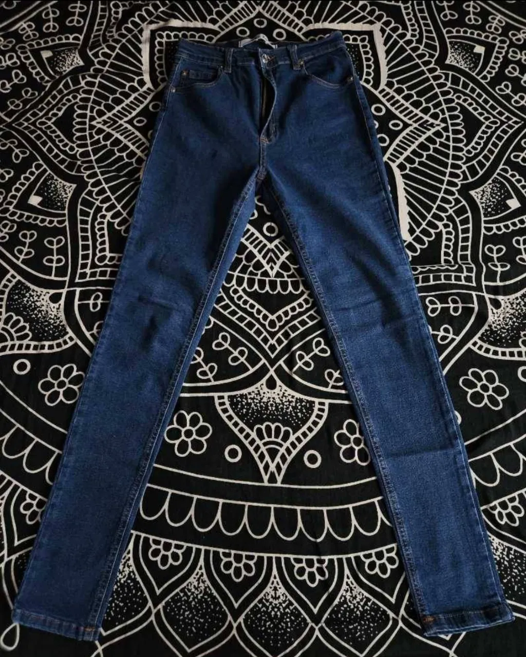 Jeans elastizado de tiro alto, color azul oscuro, con detalles de tachas en uno de los bolsillos traseros. Cierre y botón metálico. Chupin.