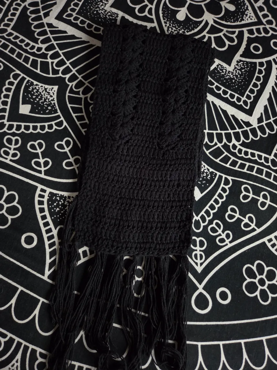Bufanda tejida en crochet, de color negro, con flecos largos en sus extremos.