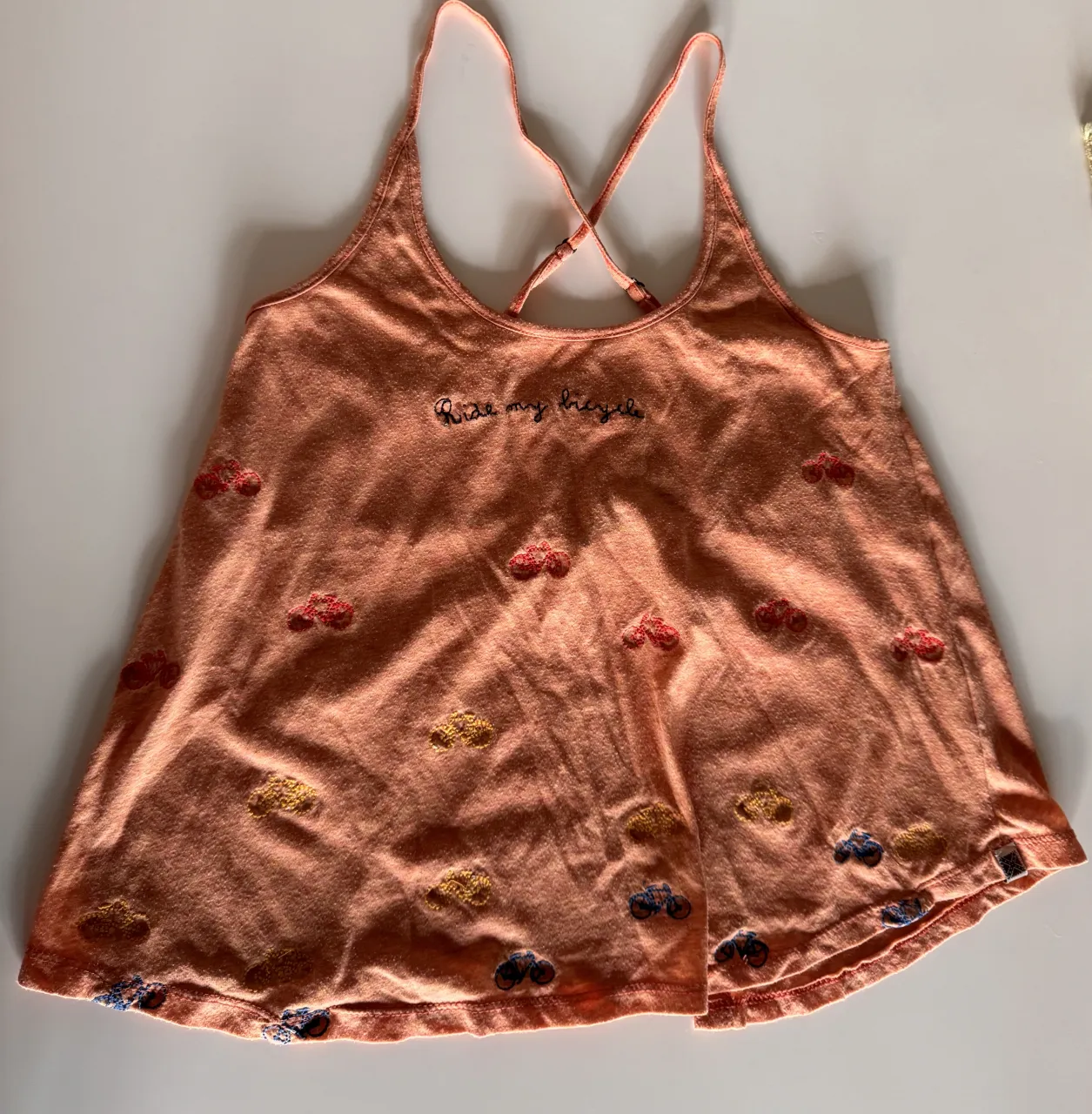 Musculosa de algodón color salmón clarito con estampa de bicicletas bordadas y la frase "Ride my bicycle". Tiene breteles cruzados en la espalda y es abierta atrás 